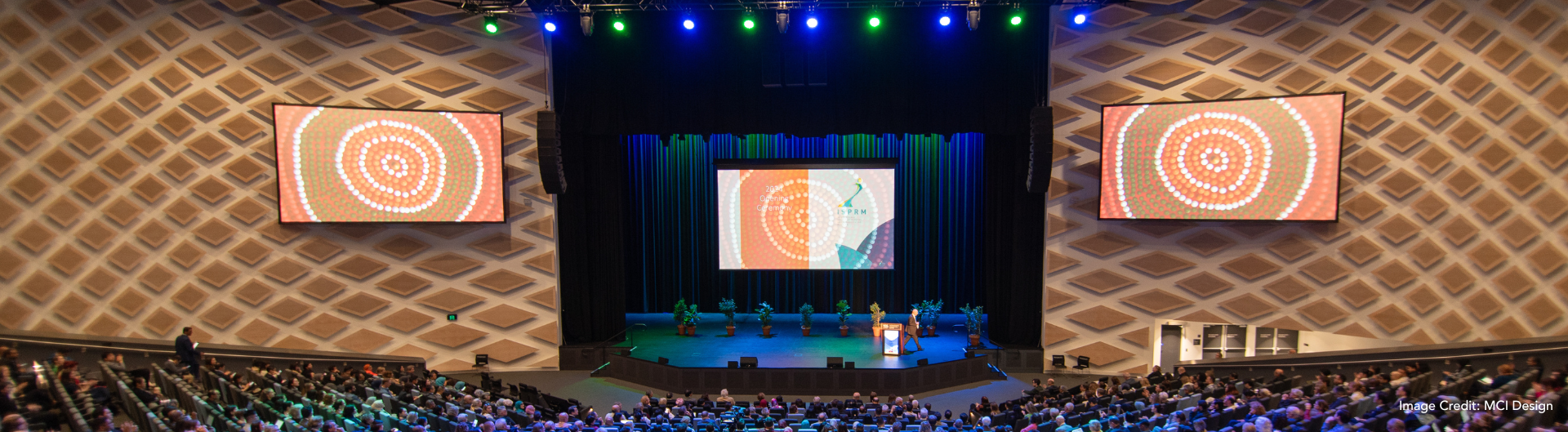 ISPRM 2024 World Congress at ICC Sydney's Darling Harbour Theatre. Shot from the back of the theatre, with First Nations art displayed on the accompanying screens to the stage.