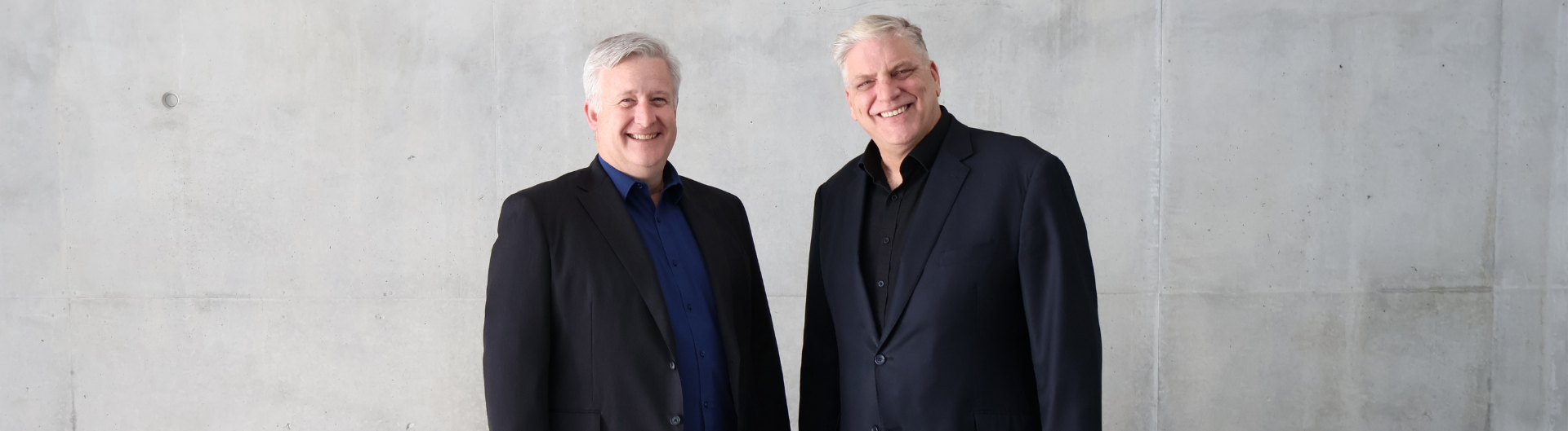 ICC Sydney's Travis Henry and Adam Mather-Brown smiling at the camera, against a concrete grey wall.